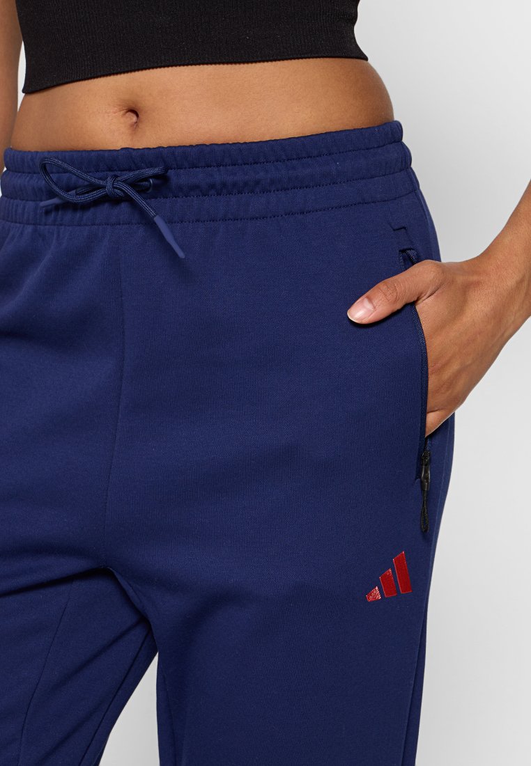Granatowe dresy wykonane z mieszanki bawełny, z elastycznym paskiem na sznurku, bocznymi kieszeniami oraz czerwonymi akcentami z logo Adidas.