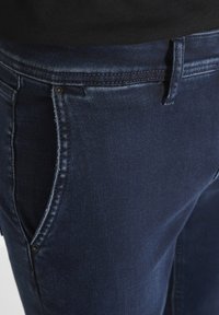 Vaqueros de mezclilla azul oscuro con una textura suave, con un corte recto, bolsillos frontales y herrajes de botón metálico en la cintura.