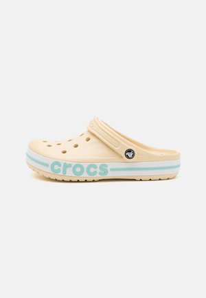 Beige Crocs klompen met ventilatiegaten, verstelbare band en lichtblauwe "crocs" branding aan de zijkant. Lichtgewicht, rubbermateriaal.