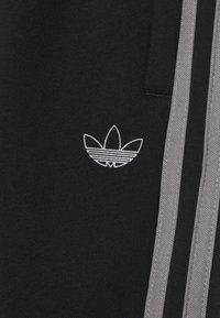 Svarta sweatpants med en vit broderad logga med tre blad och grå sidoremsor för extra kontrast. Mjuk tygstruktur.