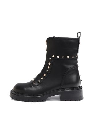 Bota de piel negra hasta el tobillo con suela gruesa, cremallera lateral y tachuelas decorativas redondas de metal en la parte delantera y trasera.