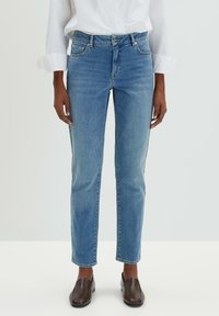 Jeans en denim bleu clair avec une coupe droite, un design à cinq poches et une légère décoloration. Associés à des chaussures à enfiler marron foncé.