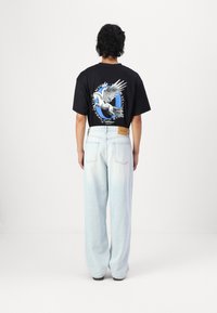 Black graphic t-shirt with a winged horse design on the back, paired with light blue wide-leg jeans and a tan leather patch on the waistband.
