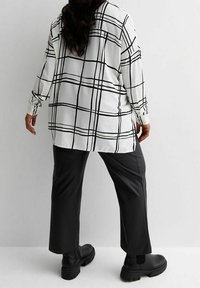 Camicia bianca con motivo a quadri neri, maniche lunghe e vestibilità ampia, abbinata a pantaloni neri a gamba larga e stivali neri chunky.