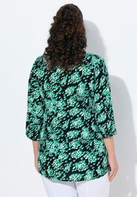 Tunic nera con motivo floreale verde e bianco, maniche a tre quarti e orlo arrotondato. Realizzata in tessuto leggero con una texture morbida.