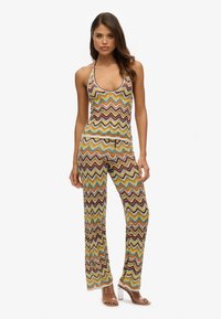 Ensemble composé d'un haut à bretelles en tissu doux avec un motif en zigzag coloré et d'un pantalon, accompagné de sandales à talons transparentes de couleur marron clair qui complètent la tenue.