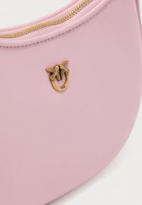 Ροζ δερμάτινη τσάντα με καμπυλωτό σχήμα, με χρυσό φερμουάρ και διακοσμητικό χρυσό στοιχείο που μοιάζει με δύο πουλιά.