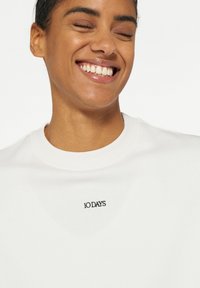 Witte sweatshirt met een ronde halslijn, voorzien van een zwart "10 DAYS" logo op de borst. Gladde textuur en casual ontwerp.