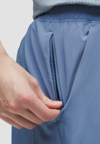 Lyseblå sportshorts med elastisk talje har en sidelomme med lynlås. Blødt, glat stof med minimale sømme.