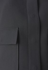 Czarna tkanina o gładkiej fakturze z wyraźną kieszenią i pionowym szwem, tworząca uporządkowany, minimalistyczny projekt.