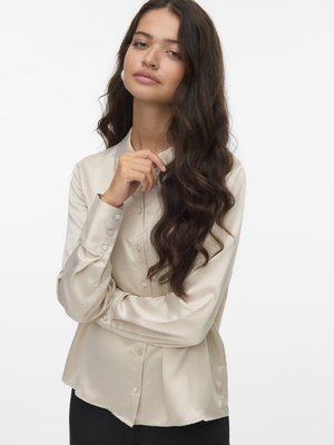 Beige satin blouse with long sleeves, button front, and a slight flare at the hem. Features a smooth texture and classic collar.