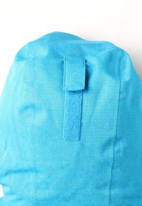 Blå tygryggsäck med en strukturerad yta, utrustad med ett vertikalt kardborreband på sidan för säker stängning. Enkelt design, utan mönster.