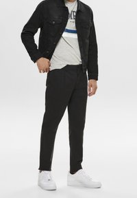 Svart denimjacka, grå t-shirt med blå rand, svarta chinos och vita sneakers. Ooutfiten har en avslappnad, lager-på-lager-design.