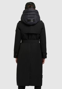 Manteau noir long avec une capuche noire rembourrée, taille ceinturée, poignets boutonnés et une fente à l'arrière. Texture lisse avec un design minimaliste.