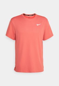 Coral Nike t-shirt made of smooth fabric, featuring a round neckline, short sleeves, and a white logo on the chest.