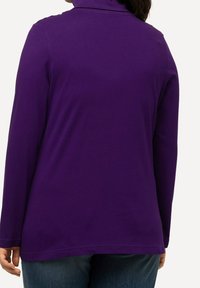 Lila långärmad polotröja i mjukt tyg. Har en avslappnad passform med rundad nederkant och minimala sömsdetaljer vid ärmsluten.