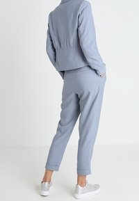 Jasnoniebieski, dopasowany garnitur z krótką marynarką i zwężanymi spodniami, wykonany z fakturowanej tkaniny. Połączony ze srebrnymi trampkami.