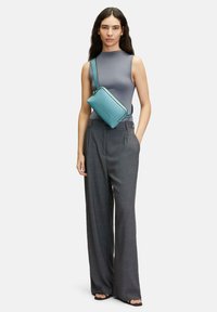 Borsa a tracolla in pelle blu con chiusura a zip, accentuata da rifiniture nere. Indossata con un top grigio senza maniche e pantaloni grigi a vita alta.