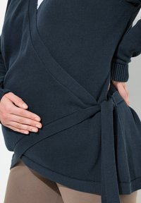 Námořnický svetr s wrap style, vyrobený z texturované pleteniny, s detailem vázání a hlubokým V výstřihem, s dlouhými rukávy a asymetrickým lemem.