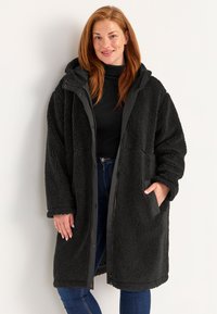 Zwarte, fuzzy sherpa jas met een capuchon, rits- en drukknoopsluiting, zijzakken en contrasterende afwerking. Zachte textuur en knielange ontwerp.