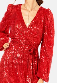 Red sequined wrap dress with long puff sleeves and a deep V-neck. Features a tied waist detail and a smooth, textured finish.