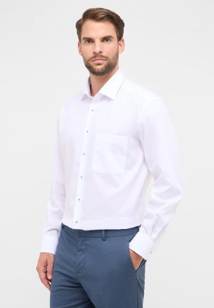 Witte longsleeve shirt met een button-down kraag, voorzien van een enkele borstzak en metalen knopen, gedragen met blauwe broek.