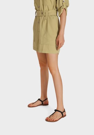 Sandali neri piattaforma con design intrecciato, sottili cinturini e suola marrone, indossati con un vestito khaki a bottoni.