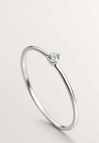 Anillo de metal plateado con un pequeño diamante redondo engastado en una montura de cuatro garras, con una banda delgada y elegante y acabado pulido.