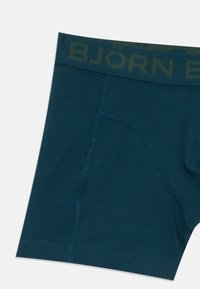 Temno teal bokserice z vidnimi šivi in elastičnim pasom, na katerem je delno viden napis "BJÖRN".