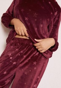 Maroonový atrakční set z manšestru, který obsahuje hvězdné vzory, dlouhé rukávy a elastický pas, s jemným texturovaným povrchem.