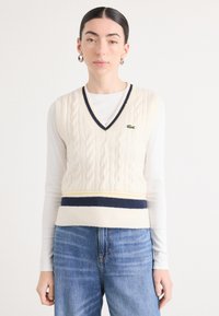 Cremfarbener Strickvest mit V-Ausschnitt, marineblauen und gelben Streifen an der Taille, mit einem kleinen grünen Logo auf der Brust.