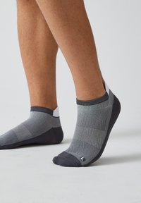 Knöchelsocken in einem gradienten Grau mit einem strukturierten Muster, ausgestattet mit einer schwarzen Spitze und Ferse sowie einem kontrastierenden weißen Bündchen am Knöchel.