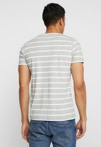 T-shirt rayé gris avec des rayures horizontales blanches, doté d'un col rond et de manches courtes, associé à un jean en denim bleu.