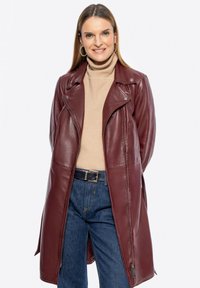 Giacca in pelle bordeaux con design aderente, chiusura con zip e accessori in argento. Combinata con un dolcevita beige e jeans in denim blu.