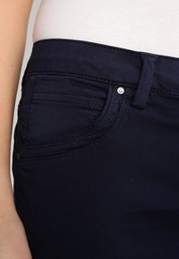 Granatowe dżinsy o slim fit, z płaskim pasem, delikatnym przeszyciem oraz przednią kieszenią z metalowym akcentem.
