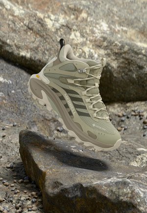 Chaussure de randonnée Merrell beige et grise avec tissu Gore-Tex, flottant au-dessus d'un terrain rocheux en plein air.