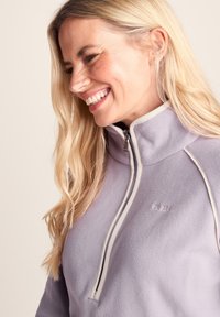 Light purple fleece pullover with a high collar, half-zip front, and white accent piping along the seams. Soft, textured fabric.