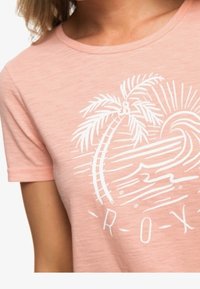 T-shirt rose à manches courtes avec un motif blanc représentant des palmiers, des vagues et le soleil. Encolure arrondie et tissu doux et texturé.