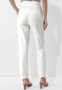 White high-waisted trousers feature a smooth texture, tapered legs, and a rear zip. Paired with light brown high-heeled sandals.