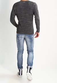Szary, teksturowany sweter z długim rękawem i okrągłym dekoltem, zestawiony z jasnoniebieskimi obcisłymi dżinsami oraz czarnymi trampkami za kostkę z białymi akcentami.