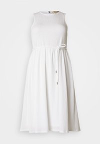 Robe blanche sans manches avec un tissu texturé. Elle présente une taille cintrée avec une fine ceinture et deux accents métalliques. Forme en A.