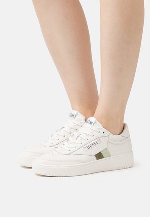 Baskets synthétiques blanches avec une finition texturée, présentant une bande verte et vert olive ainsi qu'une étiquette de marque sur le côté.