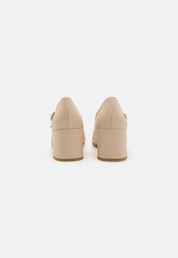 Chaussures à talons beiges avec un dessus en cuir lisse et des détails tissés ; talon carré et dos arrondi avec une finition texturée.
