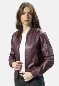 Bordeauxfarbene Lederbomberjacke mit gerippten Bündchen, seitlichen Taschen und einer Reißverschlusstasche am Ärmel. Glatte Textur und taillierte Passform.