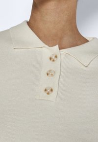 Krémový pletený polo tričko s ribbed texturou, které má na légu tři béžové plastové knoflíky.
