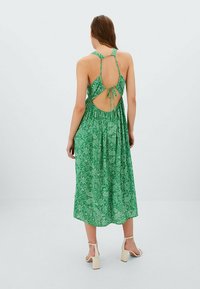 Vihreä paisley-kuosisessa mekossa on virtaava muotoilu, avoin selkä, säädettävät olkaimet ja polvenpituinen leikkaus. Kevyt kangas ja rakenne.