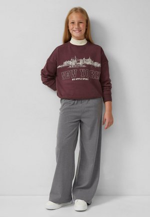 Bordeauxfarbene Baumwoll-Sweatshirt mit "NEW YORK"-Text und Skyline-Design, kombiniert mit grauen weit geschnittenen Hosen und weißen Sneakers.