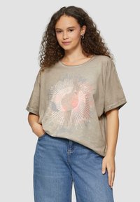 Beige T-Shirt mit kurzen Ärmeln und rundem Ausschnitt, versehen mit einem Sonnenstrahlen-Grafikdesign in Pink und Blau. Weiche, lockere Passform.