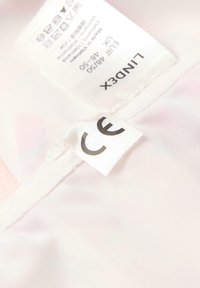 Lyserød stofmærke med plejevejledninger og størrelsesdetaljer, herunder "CE" certificeringsmærke, hængende fra plagget.