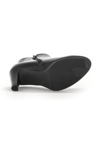 Bottine en cuir noir avec un talon courbé, une fermeture éclair sur le côté et une semelle en caoutchouc texturée. La semelle présente un motif pour une meilleure adhérence.